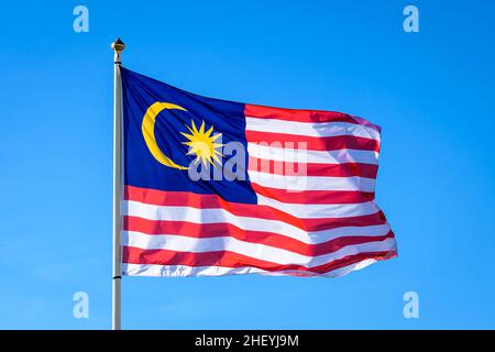 Die Nationalflagge Malaysias fliegt im Wind mit vollem Mast gegen den blauen Himmel. Stockfoto
