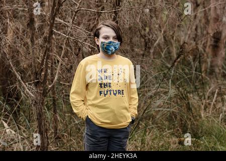 Ein Junge mit Stoffmaske und einem gelben T-Shirt, das sagt, dass „wir die Zukunft sind“ während der globalen Corona-Virus-Pandemie Covid-19 Stockfoto