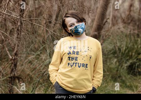 Ein Junge mit Stoffmaske und einem gelben T-Shirt, das sagt, dass „wir die Zukunft sind“ während der globalen Corona-Virus-Pandemie Covid-19 Stockfoto