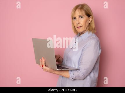 Ältere Frau, die einen Laptop benutzt, der isoliert auf einem rosa Hintergrund steht Stockfoto