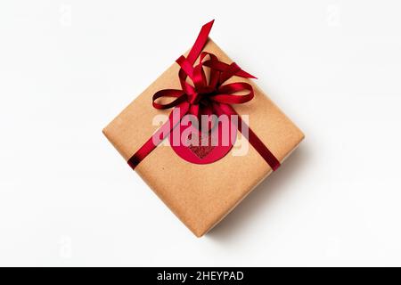 Elegantes Design der Geschenk-Geschenkbox in braunem Bastelpapier mit rotem Band und rotem Anhänger verpackt, Draufsicht auf weißem Hintergrund Stockfoto