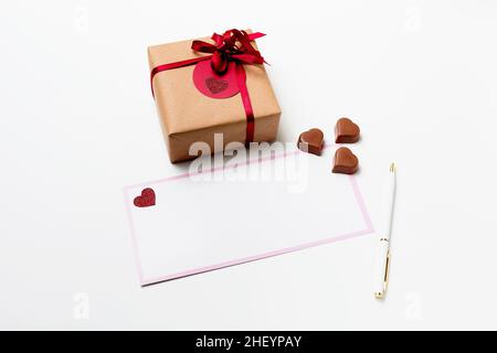 Romantisches Geschenk-Geschenkbox, weiße leere Grußkarte mit Stift und herzförmigen Schokolade Bonbons auf weißem Hintergrund Stockfoto