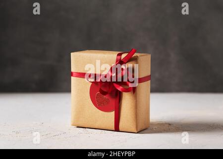 Valentinstag Geschenk-Box in braunem Bastelpapier mit rotem Band und rotem Tag verpackt, Seitenansicht Stockfoto
