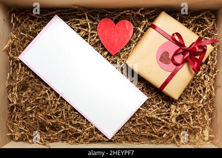 Holzkiste mit Geschenk, eingewickelt in braunem Bastelpapier mit rotem Band, mit leerer, leerer Karte, Draufsicht von oben Stockfoto
