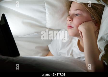 Porträt eines Mädchens mit Tablet unter der Decke in der Nacht. Gadget Night. Sucht nach sozialen Medien. Online-Kommunikation. Stockfoto