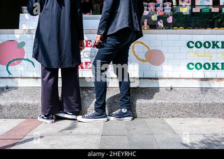 Ein romantisches Paar mit gleichfarbigen Klamotten, die zusammen stehen, kauft ein paar Kekse auf dem Bürgersteig oder einem Lebensmittelhändler auf der Straße Stockfoto