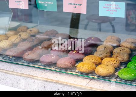 Leckere und leckere gebackene bunte Kekse auf der schwarzen Stahl-Grillmatte im Glas-Food-Case Stockfoto