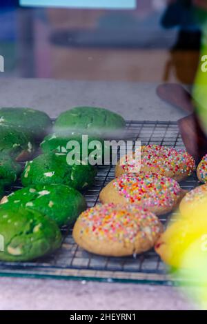 Leckere und leckere gebackene bunte Kekse auf der schwarzen Stahl-Grillmatte im Glas-Food-Case Stockfoto