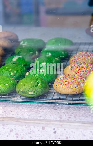 Leckere und leckere gebackene bunte Kekse auf der schwarzen Stahl-Grillmatte im Glas-Food-Case Stockfoto