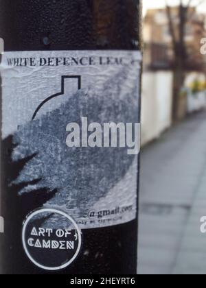 Politische Debatte durch Stellvertreter auf den Straßen von London, Großbritannien - ein Aufkleber, der die rechtsextreme White Defense League auf einem Lampenposten, zerrissen und verunstaltet, unterstützt. Stockfoto