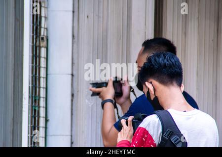 Zwei junge Fotografen, die an ihrem Job arbeiten, um mit ihren eigenen Kameras wunderschöne Aufnahmen auf dem Bürgersteig der Stadt zu machen Stockfoto