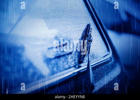 Große Regentropfen fallen vom Himmel auf die Heckscheibe des Autos. Starker Regenguss und Personentransport. Scheibenwischer. Schlechtes Wetter. Stockfoto