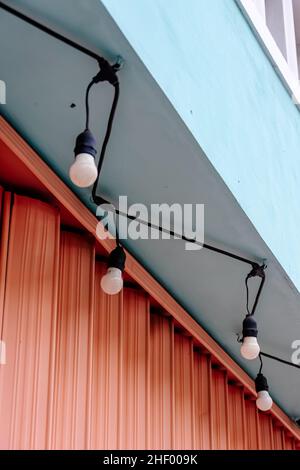 Geschlossene Ladenfront mit rosafarbenem Garagentor und den Schnur-Lampen, die an den pastellgrünen Wänden hängen Stockfoto