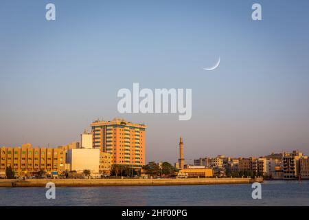 Skyline von Deira, Dubai bei Sonnenuntergang mit Dubai Creek, Moschee-Minarett und Halbmond am Himmel, Vereinigte Arabische Emirate. Stockfoto