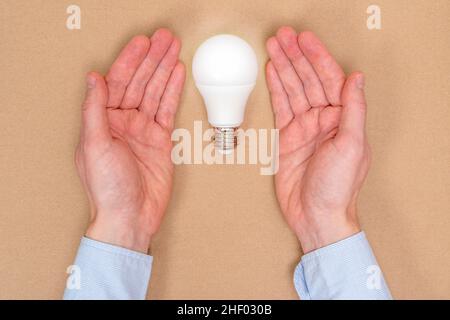 Ein Konzeptbild einer neuen Idee, einer neuen Geburt. Hände, die LED-Glühlampe bedecken. Stockfoto