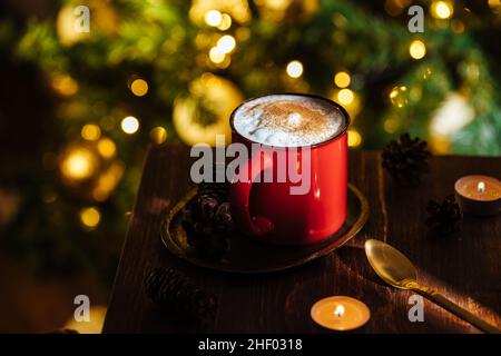 Tasse Kürbis Gewürz spät in einer rustikalen launischen und vintage Weihnachtsstimmung und Weihnachtslichter und Baum in verschwommenem Hintergrund Stockfoto