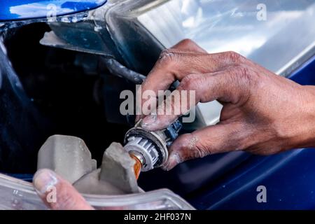 Mann Mechaniker Installation der Turn-Glühbirne mit seinen Händen in das Scheinwerferhaus des blauen Autos in der Auto-Reparatur-Garage Stockfoto