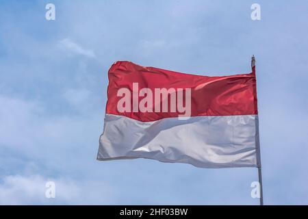 Indonesische rot-weiße Nationalflagge, die unter dem klaren und strahlend blauen Himmel aufsteigt Stockfoto