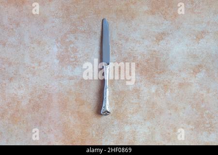 Ansicht von oben eines antiken silbernen abgerundeten Messers auf einem abstrakten pastellfarbenen Hintergrund und einer Textur. Antiquitäten und Metalle. Stockfoto