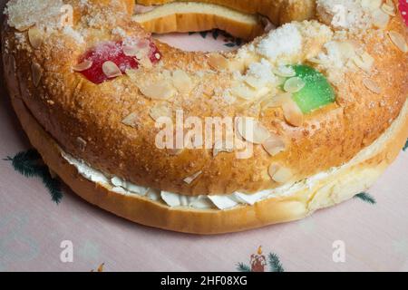 Große Donut-Kuchenfüllung mit süßer Schlagsahne mit kandierten Früchten, die die Decke auf einer dekorierten Tischdecke mit weihnachtlichen Motiven schmückt. Tradicional swe Stockfoto