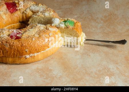 Eine Portion Roscon de Reyes Kuchen, gefüllt mit süßer Creme, die mit Mandeln, Puderzucker und kandierten Früchten verziert ist und auf einem silbernen Spuck serviert wird Stockfoto