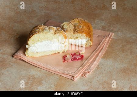 Ein Stück kandierte Frucht mit Puderzucker auf einer eleganten Serviette, begleitet von traditionellen Kuchendekorationen, gefüllt mit Creme und Mandeln auf einem Abstraktl Stockfoto