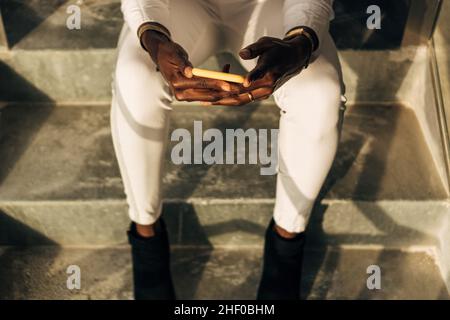 Nahaufnahme einer Frau, die ein Mobiltelefon benutzt, während sie auf einer Treppe sitzt. Stockfoto