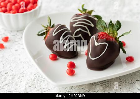 Mit Schokolade überzogene Erdbeeren auf einem Teller mit Zimt-Herzen verstreut. Stockfoto