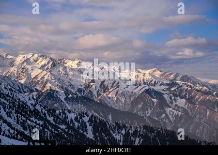 Majestätische Bergrücken, die von weichem Morgenlicht vor einem blauen Himmel mit Wolken beleuchtet werden Stockfoto