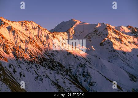 Weiches Abendlicht auf Bergkämmen; felsige Berge, die bei Sonnenuntergang mit Schnee bedeckt sind Stockfoto