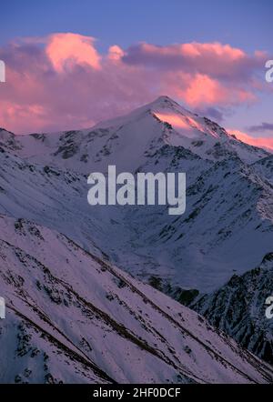 Schneebedeckte Berge bei Sonnenuntergang; Berggipfel gegen einen blauen Himmel mit Sonnenuntergangswolken Stockfoto