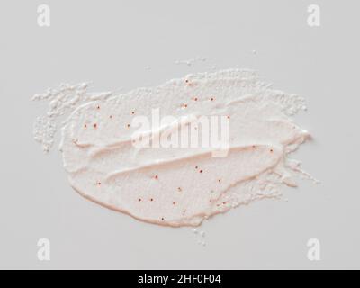 Flecken auf weißem Hintergrund. Kosmetisches Peeling mit Textur für Gesicht und Körper mit roten Schleifpartikeln in pastellrosa Farbe. Peeling Körper polieren Textur als kosmetische Gommage Hintergrund mit Kopierraum Stockfoto