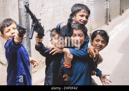 Peshawar, Pakistan - 09. Juni 2020: Fröhliche und fröhliche pakistanische Kinder, die mit Spielzeugpistolen in traditionellem Kleid spielen Stockfoto