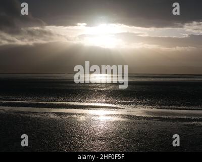 Die Sonne bricht bei Ebbe bei West Kirby auf Wirral in Nordwestengland durch Wolken über dem Watt der Dee-Mündung. Die Küste von Nordwesten Stockfoto