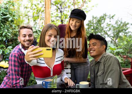 Multikulturelle, glückliche Freunde, die während einer Kaffeepause Spaß haben, ein Selfie-Portrait in der Gruppe draußen im Garten zu machen - gemischte junge Leute lachen zusammen Stockfoto