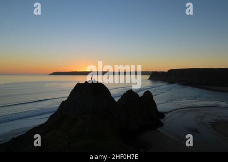 Kletterer an der Spitze der Bucht von Three Cliffs mit Sonnenuntergang hinter dem Oxwich Point in Südwales Stockfoto