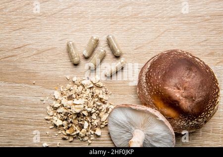 Flache Ansicht von trockenem Pulver aus Shiitake-Pilzen, Lentinula edodes. Lebensmittelzutat auf Schneidebrett aus schwarzem Stein mit frischen Shiitake-Pilzen. Stockfoto