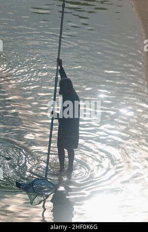 Silhouette eines mexikanischen Jungen, der an einem Sommermorgen einen öffentlichen Pool instandhalten soll Stockfoto