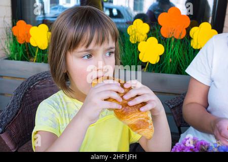 Ein Mädchen im Café isst ein Croissant. Stockfoto