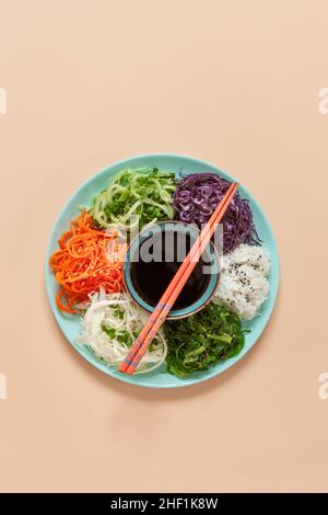 Hausgemachte vegetarische Poke-Schüssel frische rohe Karotten, Rotkohl, Gurke, Reis, essbare Algen mit Sojasauge, Ernährung, gesunde Lebensmittel auf Korallen Pastell Backg Stockfoto