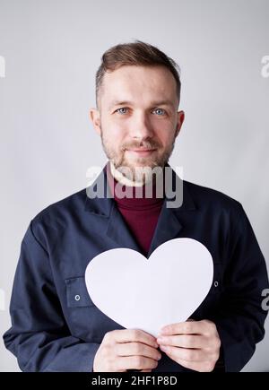 Valentinstag: kaukasischer Mechaniker, Mechaniker, Werkmeister, Auftragnehmer oder Arbeiter in Uniform lächelnd in der Liebe mit den Händen in Form eines weißen Papiers. Romantik, Beziehungskonzept. Hochwertige Fotos Stockfoto
