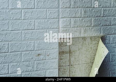 Die Tapete beginnt sich abzulösen. Die Tapete aus alten weißen Ziegeln schälte sich von der Wand im Raum, weil es feucht war oder sich nicht gut klebte. Reparieren Sie A Stockfoto
