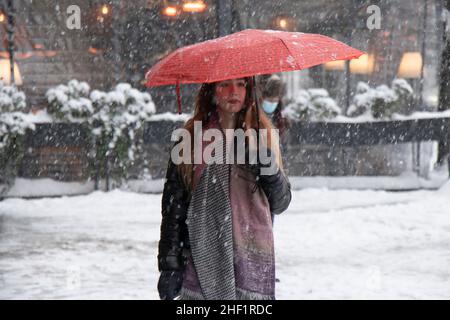 Belgrad, Serbien - 11. Januar 2022: Eine junge Frau, die an einem verschneiten Wintertag in der Stadt unter rotem Regenschirm läuft Stockfoto