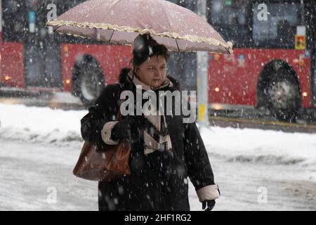 Belgrad, Serbien - 11. Januar 2022: Eine Frau, die an einem verschneiten Wintertag auf der Straße der Stadt unter dem Regenschirm läuft Stockfoto