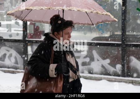 Belgrad, Serbien - 11. Januar 2022: Eine Frau, die an einem verschneiten Wintertag auf der Straße der Stadt unter dem Regenschirm läuft Stockfoto