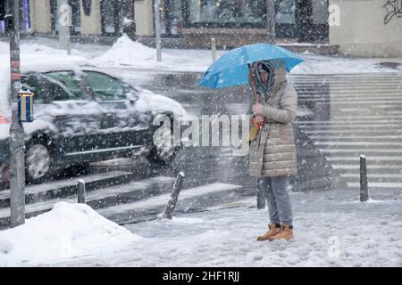 Belgrad, Serbien - 11. Januar 2022: Frau wartet an der Kreuzung unter blauem Schirm auf einer verschneiten Stadtstraße bei starkem Schneefall Stockfoto