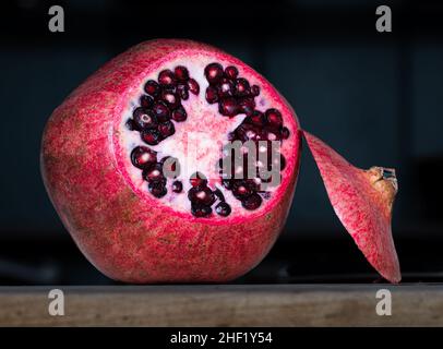 Roter Granatapfel mit abgeschnittenem Oberteil auf dunklem Hintergrund Stockfoto