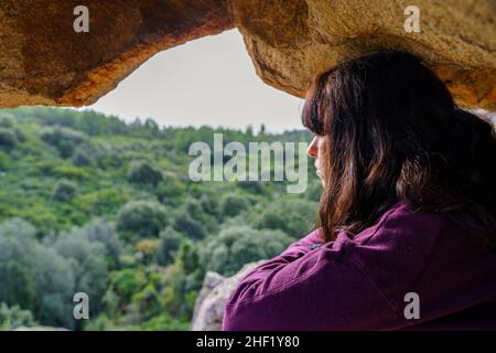 Frau, die auf einem Hügel in der Mitte einer Höhle sitzt und die Landschaft betrachtet Stockfoto