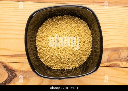 Rohe Bio-Hirse in einer schwarzen Keramikplatte auf einem Holztisch, Makro, Draufsicht. Stockfoto