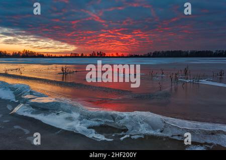 Majestätischer Sonnenuntergang im Winter mit rotem Himmel, der sich auf dem Eis des Sees spiegelt Stockfoto